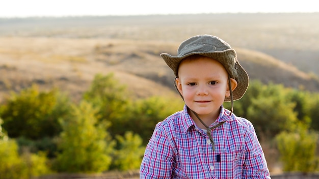 Menino com um chapéu de sol fofo posando em frente a uma bela vista do campo