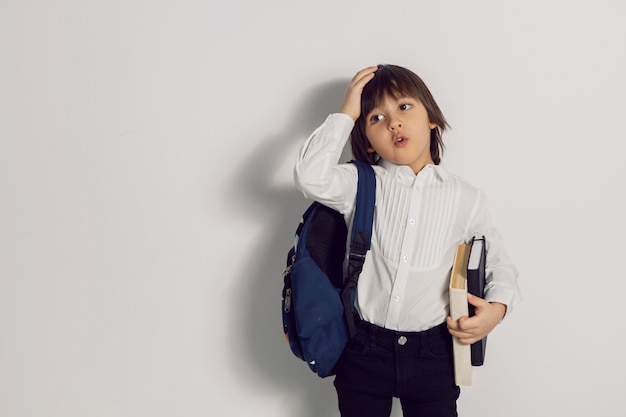 Menino com um livro e uma mochila em uma parede branca