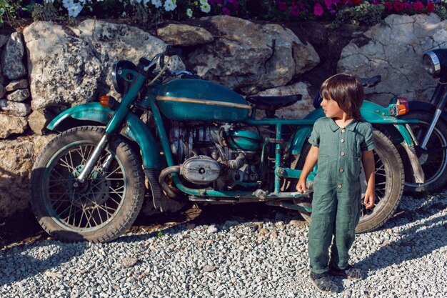 Menino com um macacão verde andando entre velhas motocicletas no verão