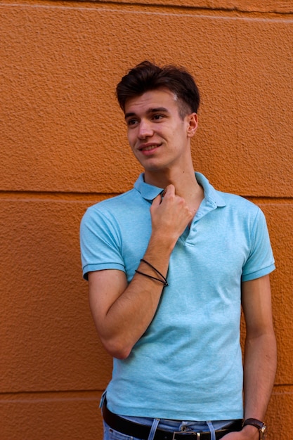 Menino com uma camisa pólo azul esperando em um fundo laranja na rua