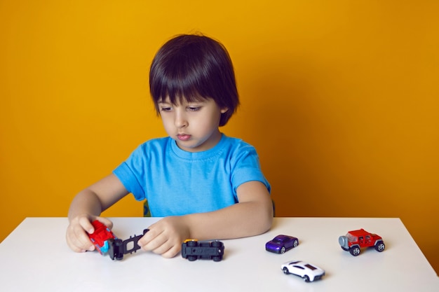 Menino com uma camiseta azul se senta a uma mesa e brinca com um carrinho de brinquedo