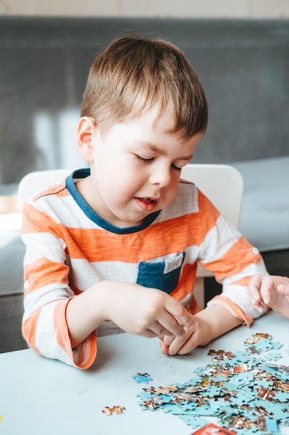 Menino com uma camiseta laranja coleta um quebra-cabeça sobre a mesa. tempo sem gadgets. jogos de tabuleiro para crianças. O menino desenvolve habilidades motoras finas e cérebro