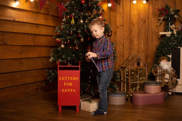 Menino com uma carta para o Papai Noel na caixa de correio de Natal.