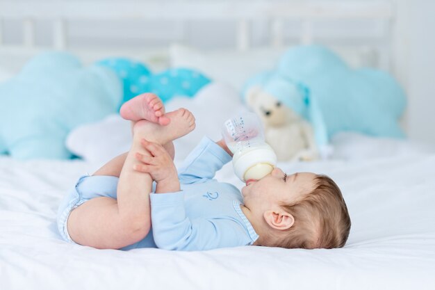 Menino com uma garrafa de leite na cama para dormir com uma roupa azul, conceito de comida de bebê