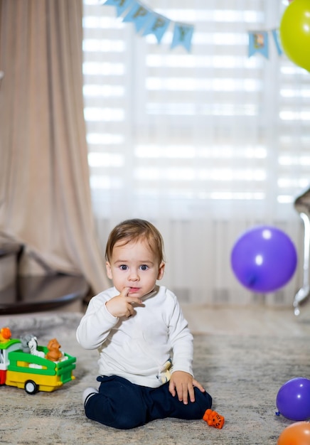 Menino comemora seu primeiro aniversário em torno de bolas e presentes Menino bonito brincando com balões coloridos