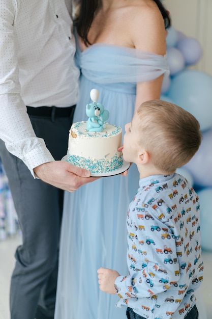 Menino comendo seu bolo de aniversário. Bolo branco e azul. Ideia de foto de família