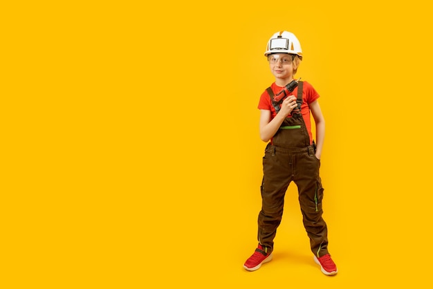 Menino como trabalhador em fundo amarelo Criança usa capacete de proteção e segura furadeira na mão Copie o espaço simulado