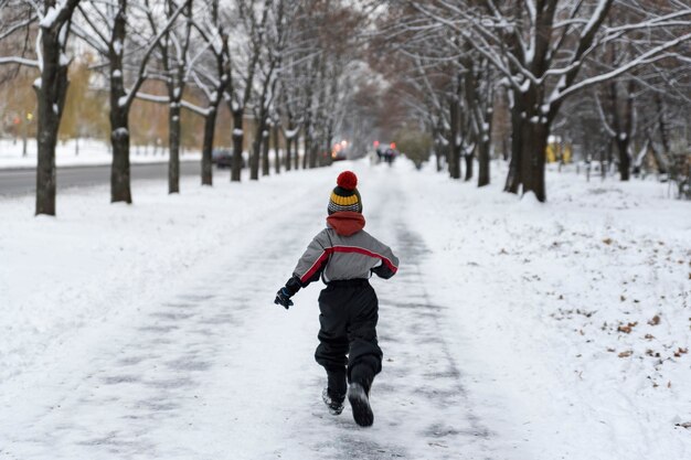 Menino corre pelo parque no inverno. Vista traseira. Criança caminha no parque nevado.