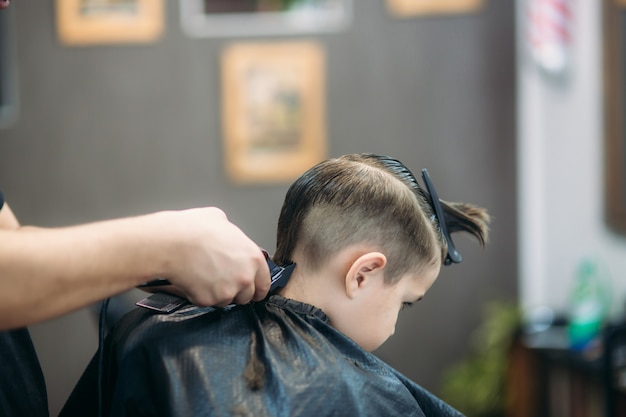 Menino cortando o cabelo de barbeiro enquanto está sentado na cadeira de barbearia.