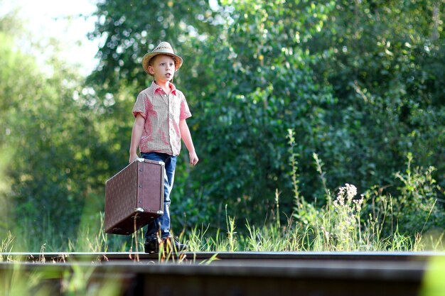Menino cowboy com uma mala esperando um trem e uma ferrovia conceito de viagem ocidental