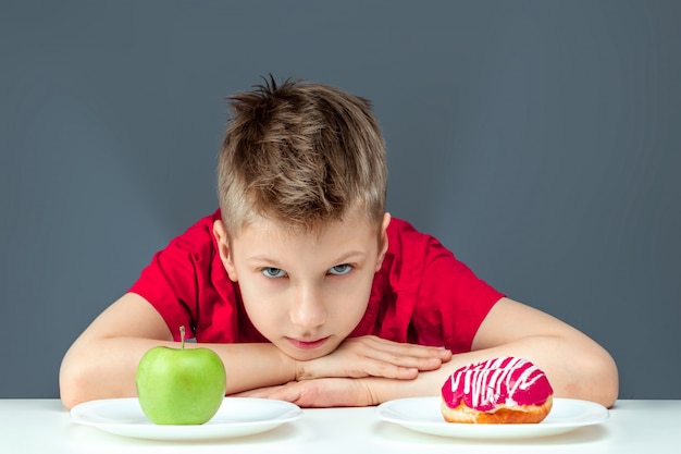 Foto menino criança escolhe entre um donut e uma maçã verde. conceito resistência à tentação, fast food, alimentação saudável, dieta.