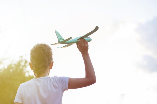 Menino criança feliz brincando com avião de brinquedo ao ar livre ao pôr do sol