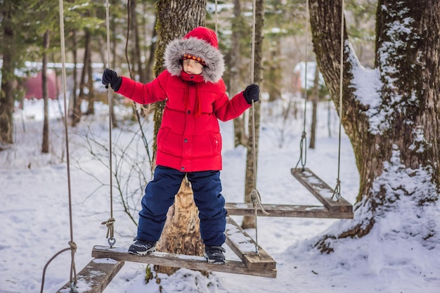 Menino criança feliz desfrutando de atividade em um parque de aventura de escalada em um dia de inverno