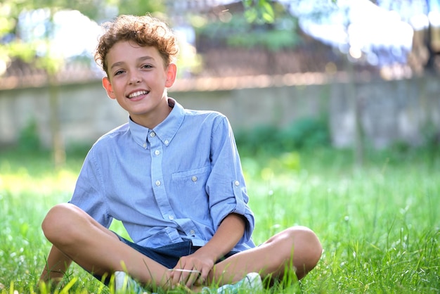 Menino criança feliz relaxando na grama verde no parque de verão Criança positiva aproveitando o verão ao ar livre Conceito de bem-estar infantil