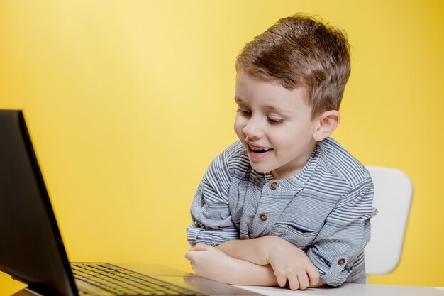 Menino criança feliz sentado à mesa com o laptop e se preparando para a escola