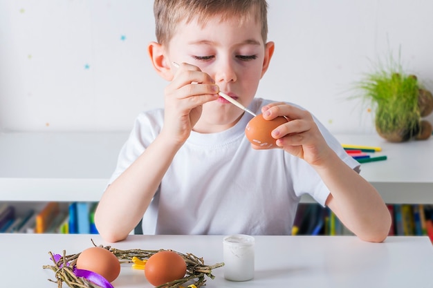 Menino criança pinta ovos com tinta branca. conceito de diy.