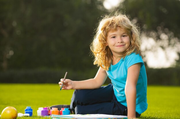 Menino criança pintando na natureza da primavera Crianças escolares desenhando no parque de verão pintando arte Pequeno pintor