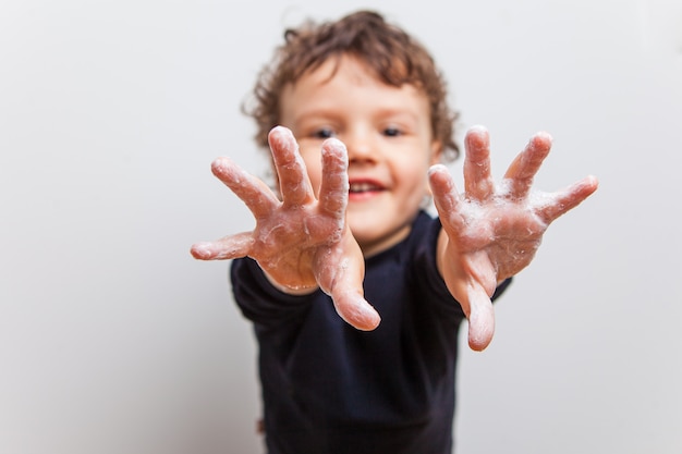 Foto menino, criança puxa as mãos ensaboadas para a frente