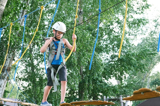 Menino criança se divertindo de verão no parque de aventura na tirolesa. Traves de equilíbrio e pontes de corda.