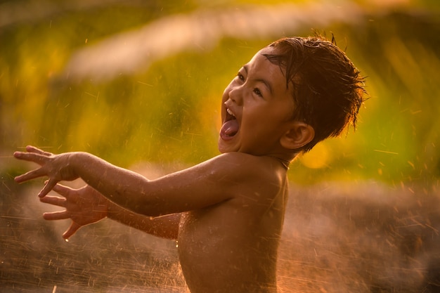 Menino da ásia, sorrindo e brincando com salpicos de gotas de água