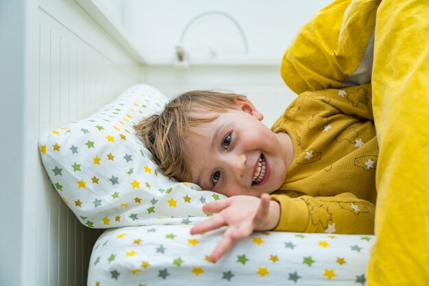 Menino da criança está deitado na cama. criança acordando de manhã com um sorriso. criança feliz descansando em casa.