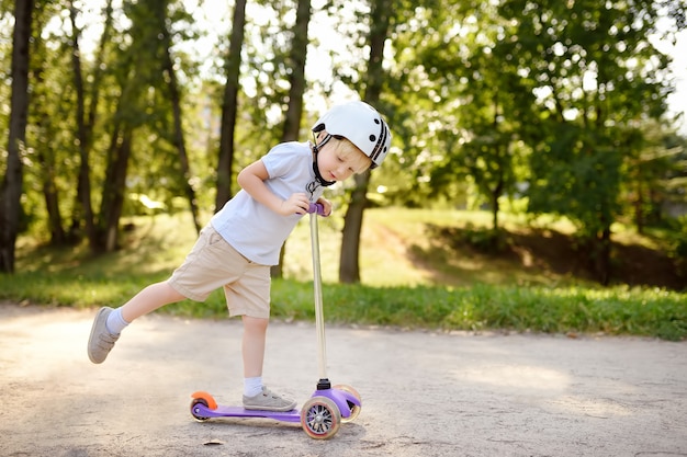 Menino da criança no capacete de segurança, aprendendo a andar de scooter