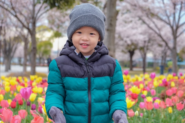 menino da criança sorrindo e olhando para a câmera na flor de cerejeira Sakura e o parque de campo de tulipas