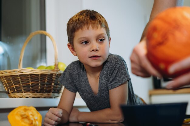 Menino de 6 anos de idade bonito caucasiano olhando para o pai esculpindo uma abóbora para fazer a lanterna tradicional de Jack. Preparação para a celebração do halloween