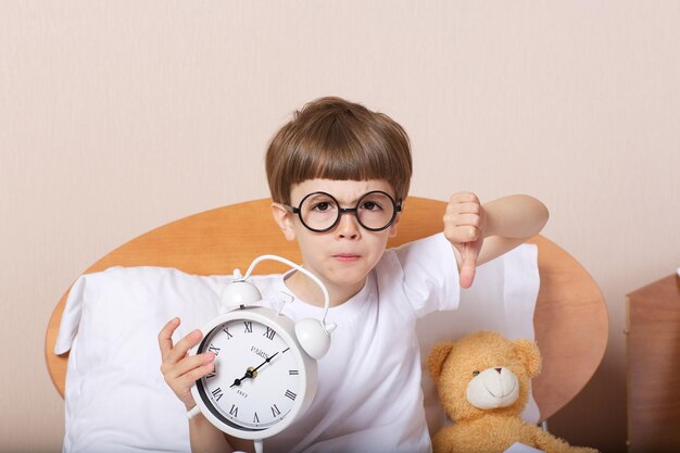 Foto menino de 6 anos na cama com grande despertador