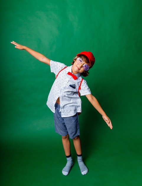 Menino de 7 anos em um fundo verde com os braços estendidos, retrato de uma criança feliz