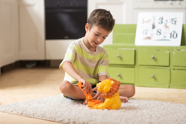 Menino de 7 anos senta no tapete e brinca com brinquedos em casa Jogos educativos