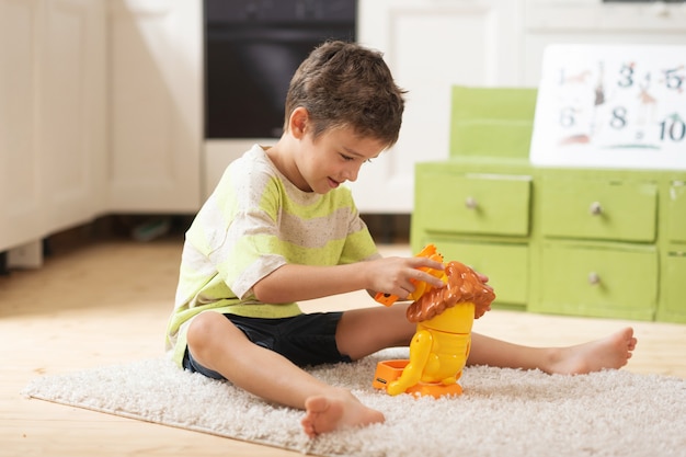 Menino de 7 anos senta no tapete e brinca com brinquedos em casa jogos educativos