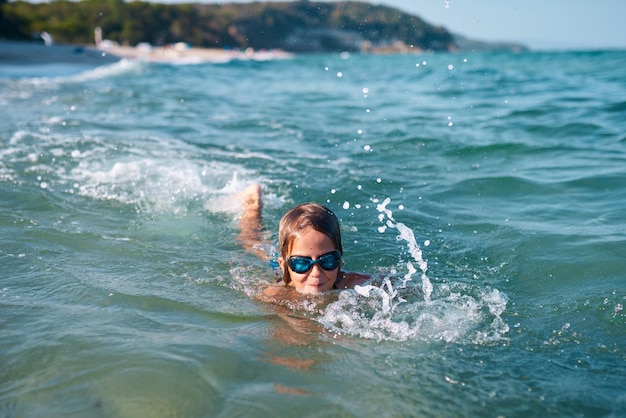 Menino de 8 anos nada no mar em óculos de natação azuis à noite