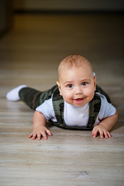 Menino de 8 meses de macacão, camisa e meias brancas rastejando no chão e sorrindo