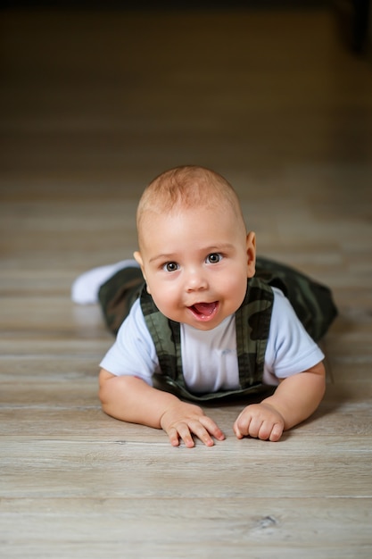 Menino de 8 meses de macacão, camisa e meias brancas rastejando no chão e sorrindo