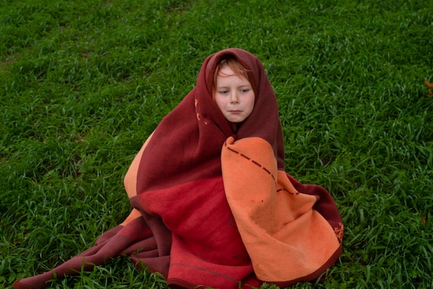 Menino de 9 anos envolto em um cobertor no campo