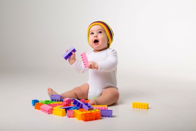 Foto menino de 9 meses brincando com um construtor multicolorido em uma parede branca