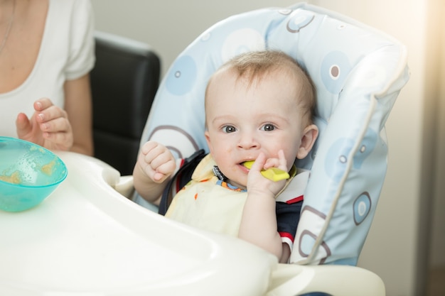 Menino de 9 meses com colher sentado na cadeira alta