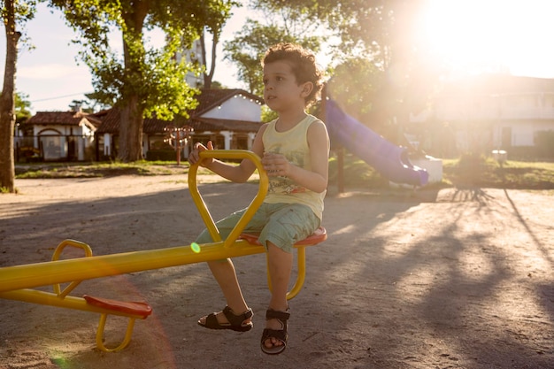 Menino de aparência caucasiana com cabelo encaracolado andando em uma gangorra no parque