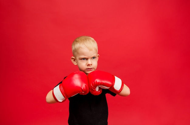 Menino de boxe agressivo com luvas de boxe vermelhas no vermelho