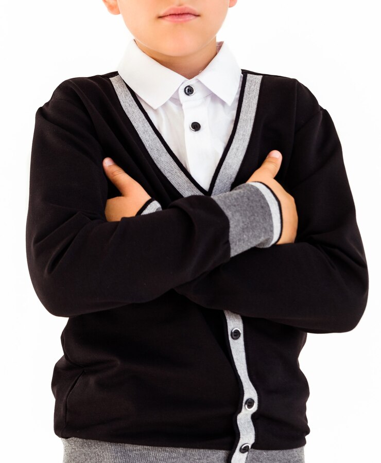 Foto menino de camisa branca e suéter preto posando em fundo branco com os braços cruzados