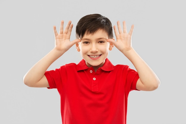 menino de camisa vermelha fazendo orelhas grandes com as mãos