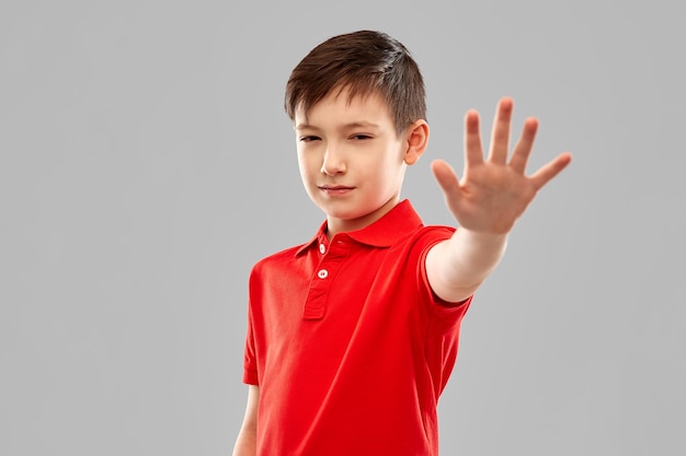 Foto menino de camisa vermelha fazendo um gesto de parada