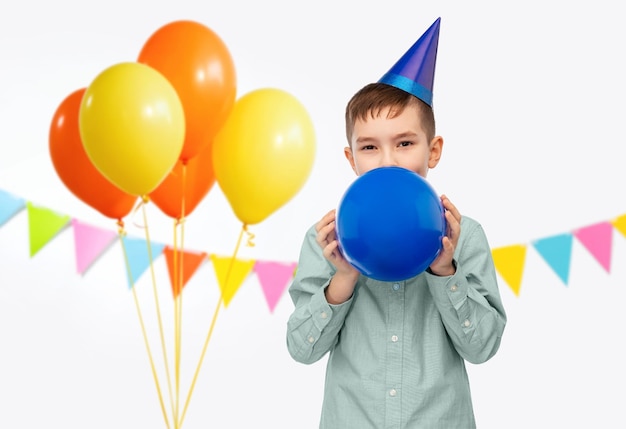 menino de chapéu de festa de aniversário soprando balão
