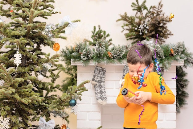 Menino de criança com petardo nas mãos perto da árvore de Natal decorada e lareira Conceito de férias aconchegantes de inverno ou ano novo Fundo de natal com foco seletivo