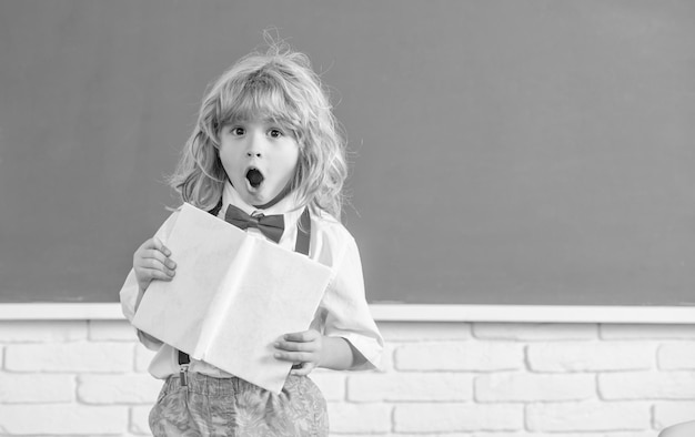 Menino de criança espantado no estudo de gravata borboleta na sala de aula da escola com espaço de cópia de notebook de volta à escola
