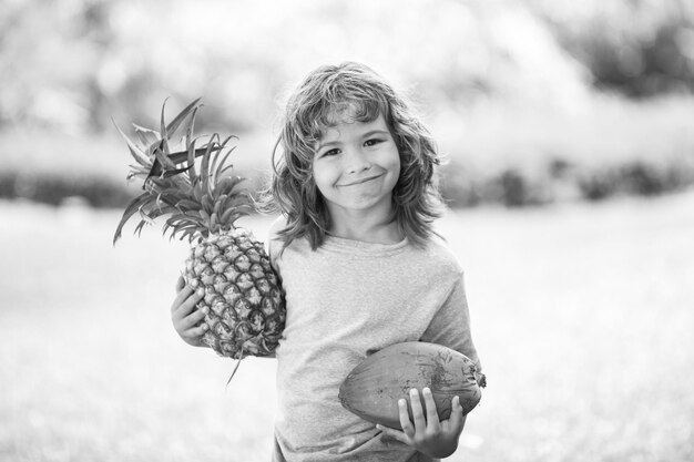 Menino de criança segurando abacaxi e coco sorrindo com cara de feliz. Frutas de verão.