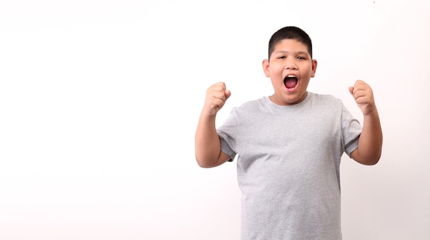 Foto menino de crianças feliz animado levantando os punhos, fazendo o gesto de sim, comemorando o sucesso em fundo branco.