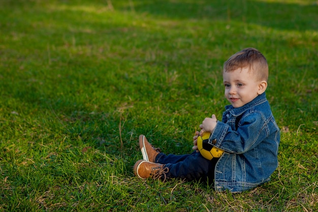Menino de dois anos segurando uma bola de futebol sentado na grama
