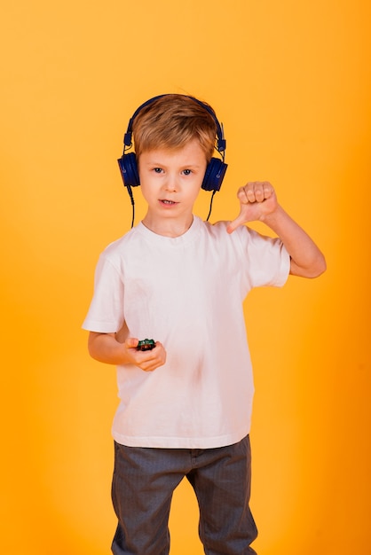 Menino de emoções ouve música com fones de ouvido em seu telefone, parede amarela.